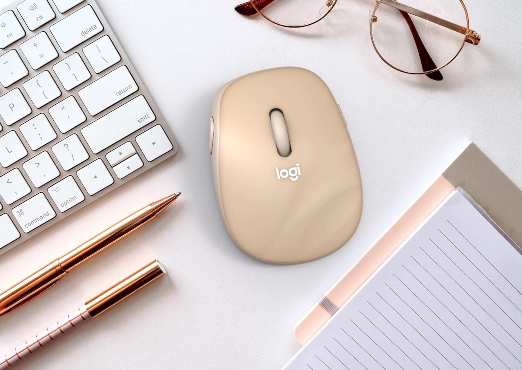 Logitech PC mouse concept in sand on a desk beside a keyboard and glasses